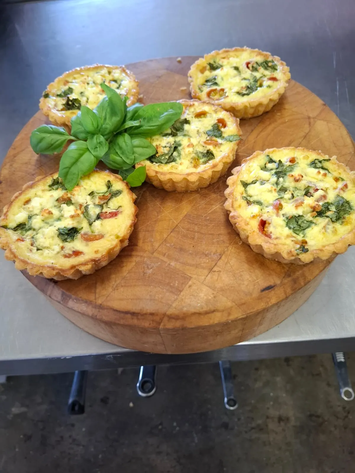 Five savoury tartlets with feta, cherry tomato and basil on a round wooden board.