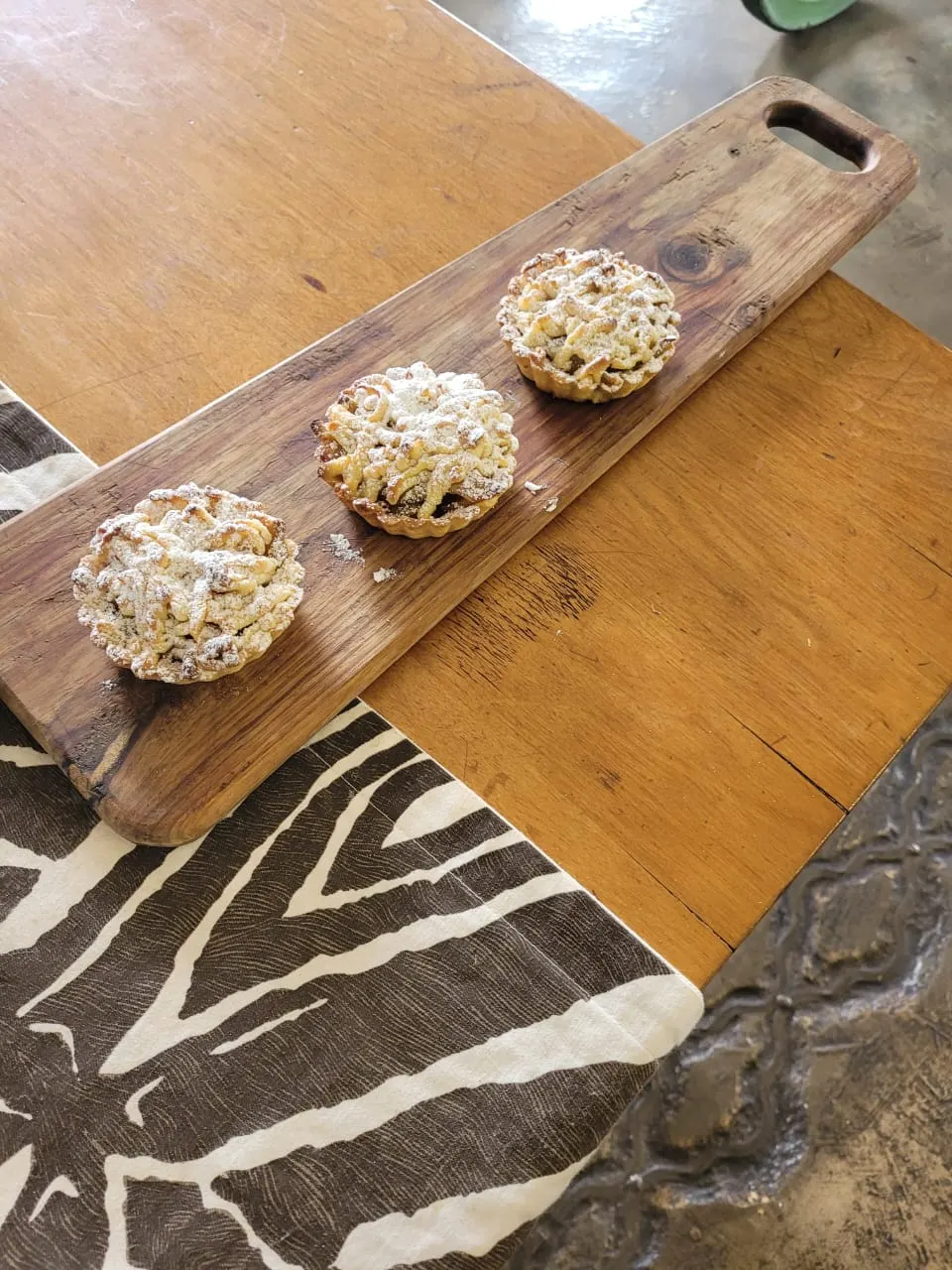 Three apple lattice tartlets dusted with icing sugar on a wooden board.
