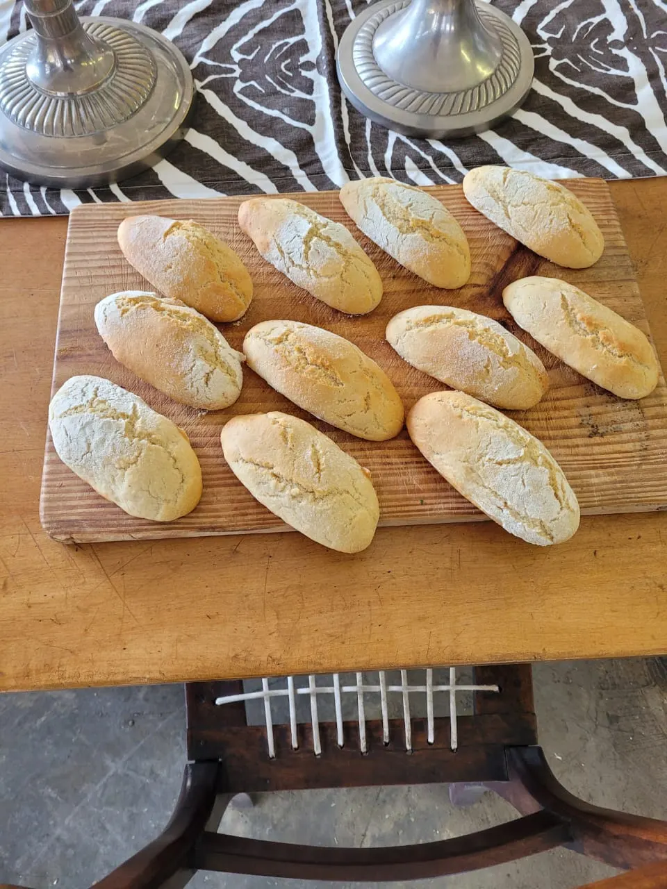 Baked bread rolls on a wooden board beside two pewter lamp bases.