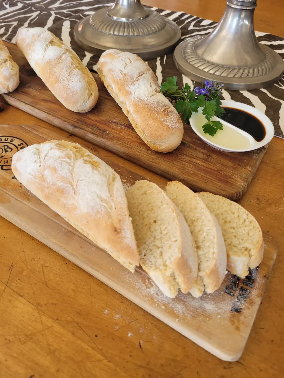 Sliced bread loaves with olive oil and balsamic dip and fresh herbs on a board.