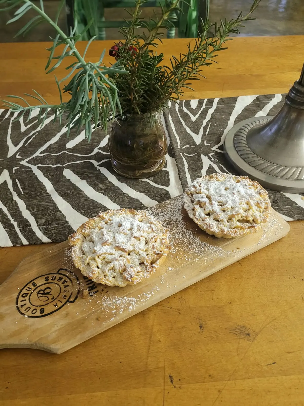 Two apple lattice tartlets on a board with a jar of rosemary.