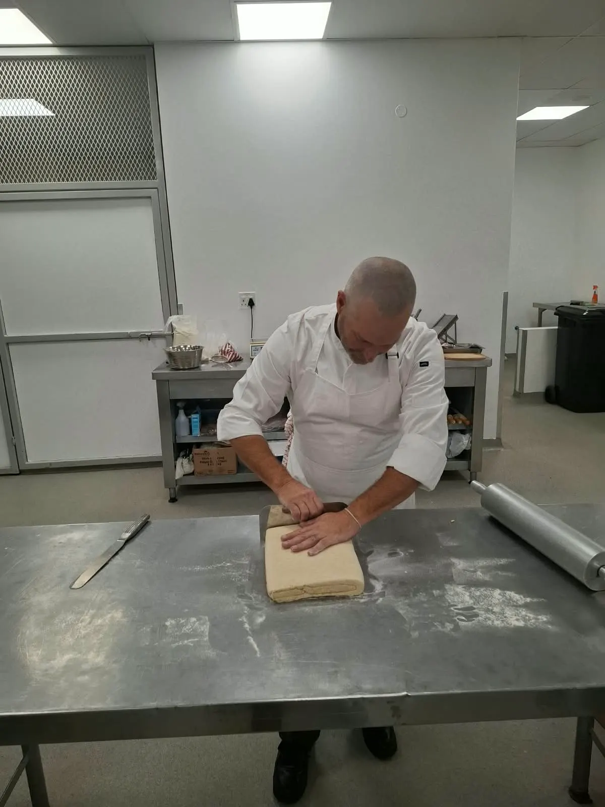 Chef folding laminated pastry dough on a floured steel bench