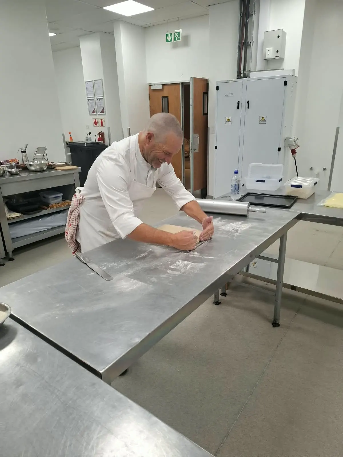 Chef shaping pastry dough by hand on a steel bench