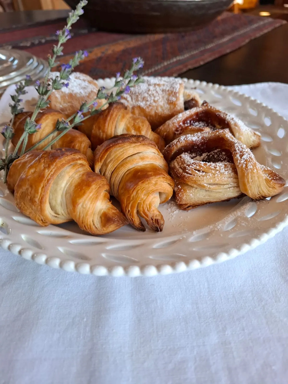 Croissants and jam-filled Danish pastries dusted with icing sugar on a white plate.