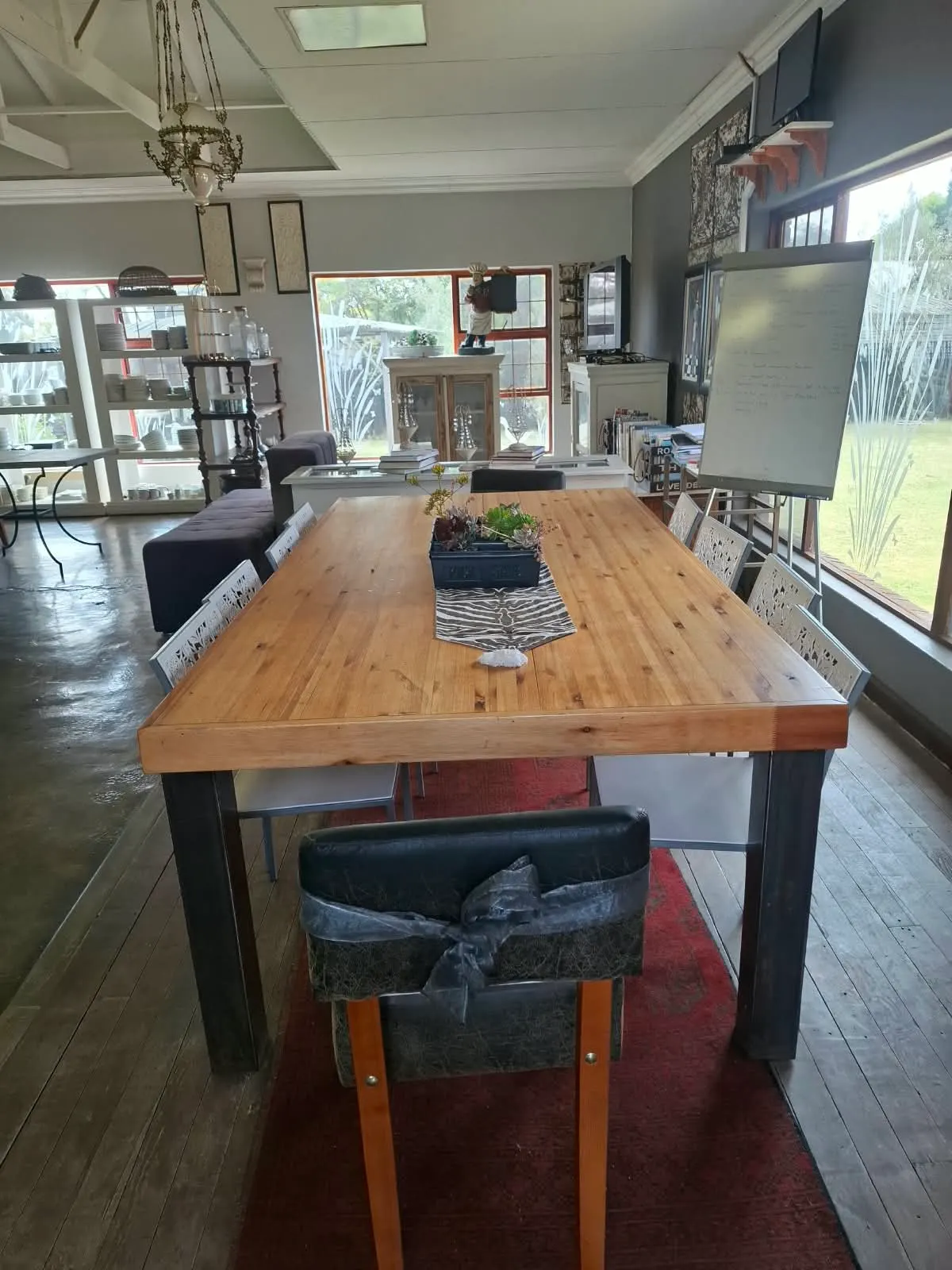 Communal wooden table beside the whiteboard and garden windows