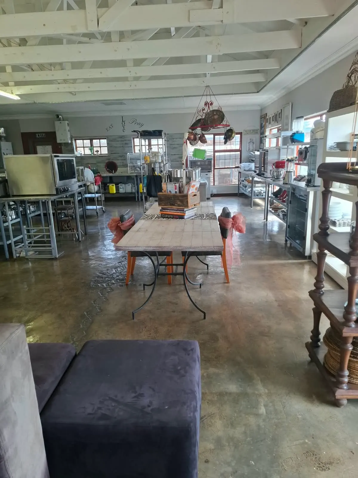Long view of the training kitchen with a communal table and equipment shelves
