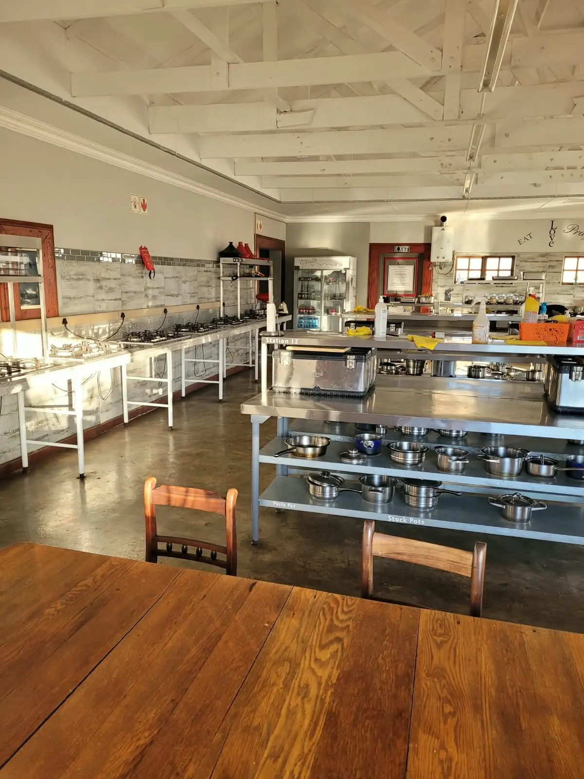 Cooking stations and steel prep benches in The Chef School's training kitchen, lit by afternoon sun