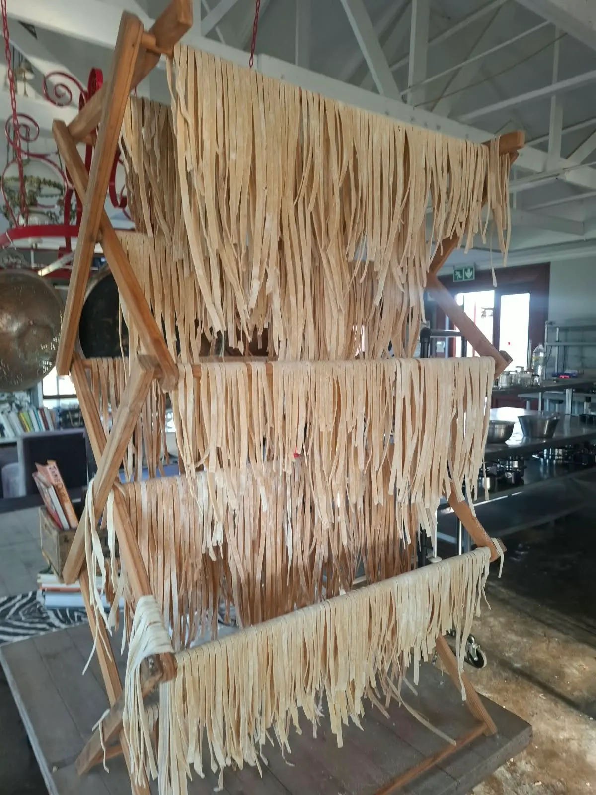Fresh pasta ribbons hanging to dry on a wooden rack in the training kitchen.