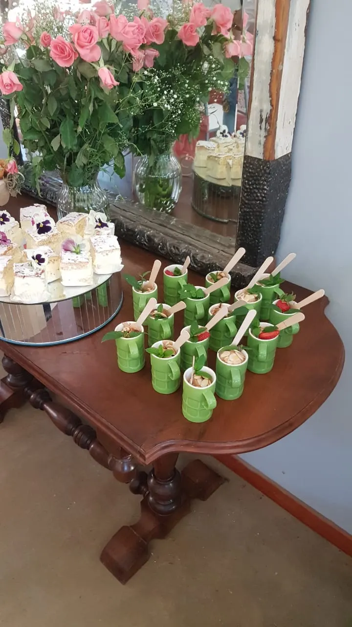 Mini dessert cups with strawberries and almonds beside custard slices and pink roses