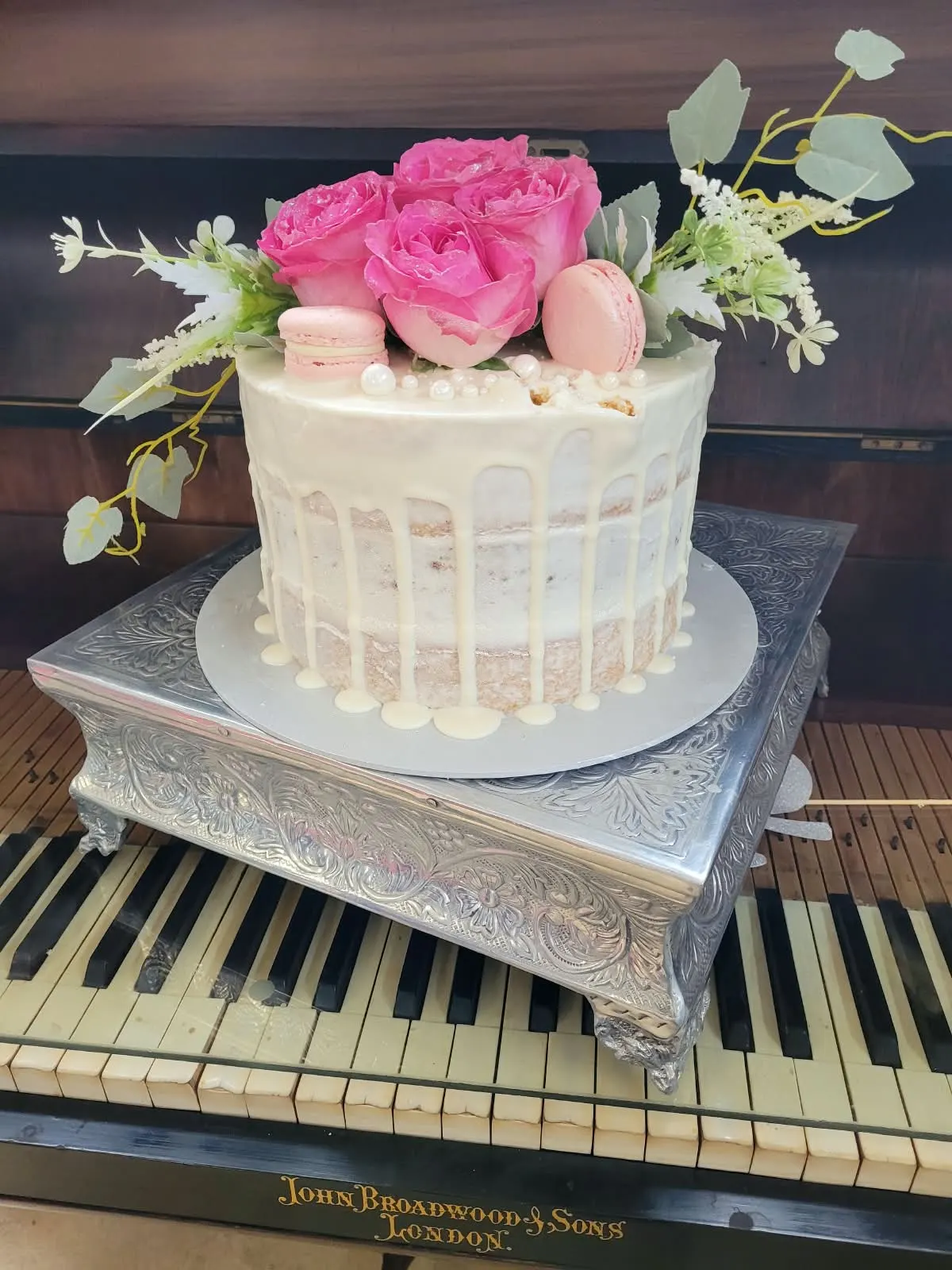 Naked cake with white chocolate drip, pink roses and macarons on a silver stand